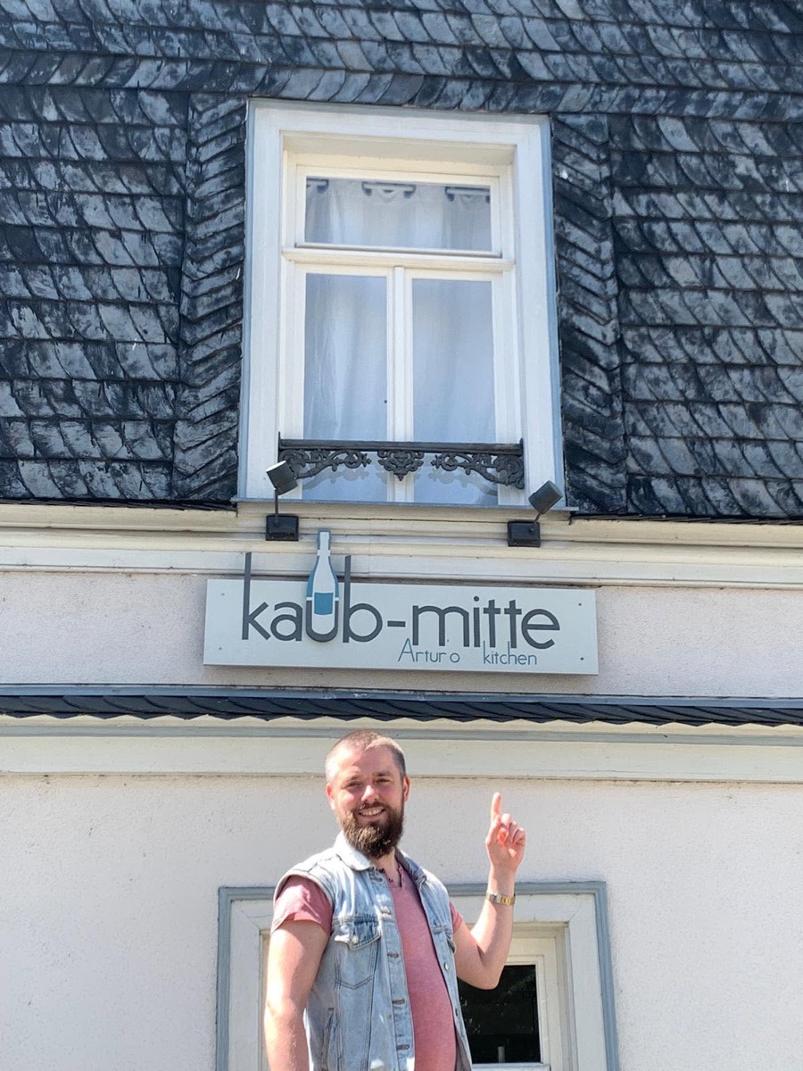 Artur Judickij zeigt lächelnd auf das Schild seines Restaurants